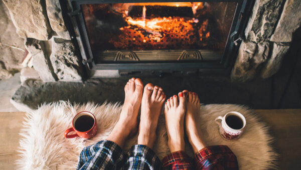 A couple's bare feet resting in front of cozy fireplace